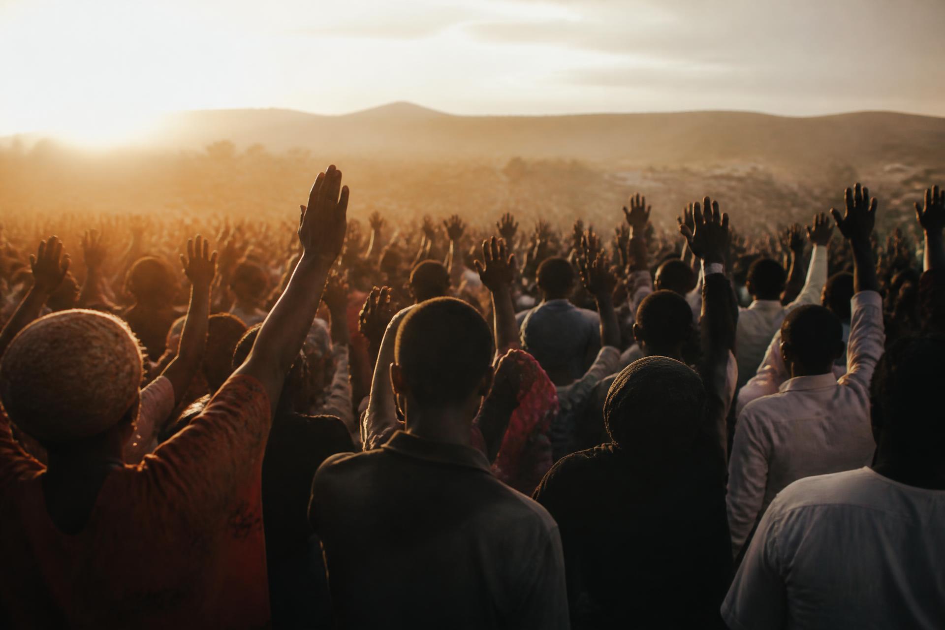 Worshippers with hands raised at an outdoor Christian gathering at golden hour